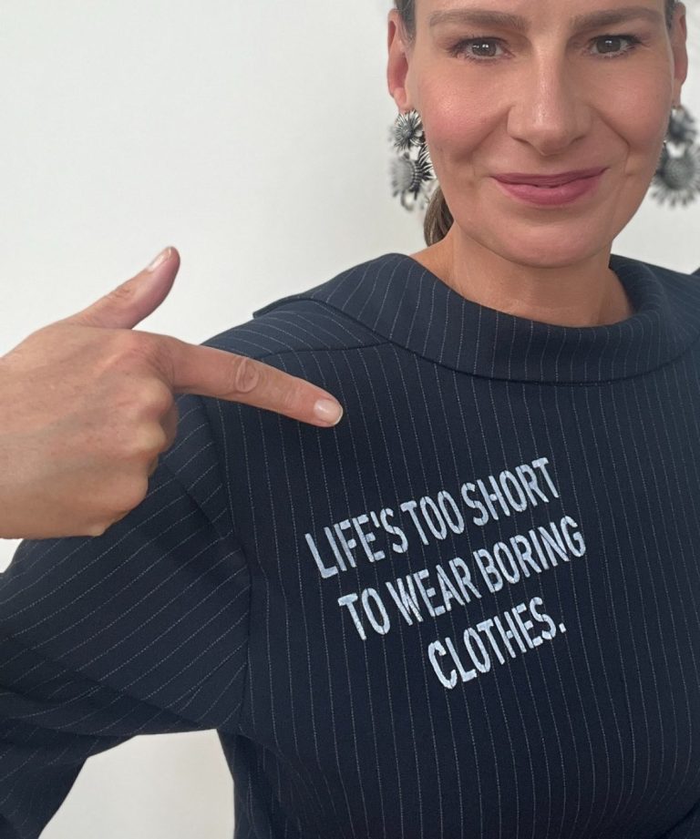 Motto vom Buero fuer Strahlkraft Ellen Schmitt zeigt auf ihr Oberteil mit dem Spruch „Life's too short to wear boring clothes.“